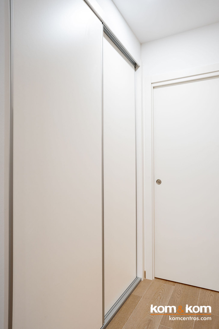 Armario empotrado a medida con puertas correderas en acabado blanco liso, dise&ntilde;ado por Kom&Kom para maximizar el aprovechamiento de espacio en la entrada de apartamentos tur&iacute;sticos Emily Suits.